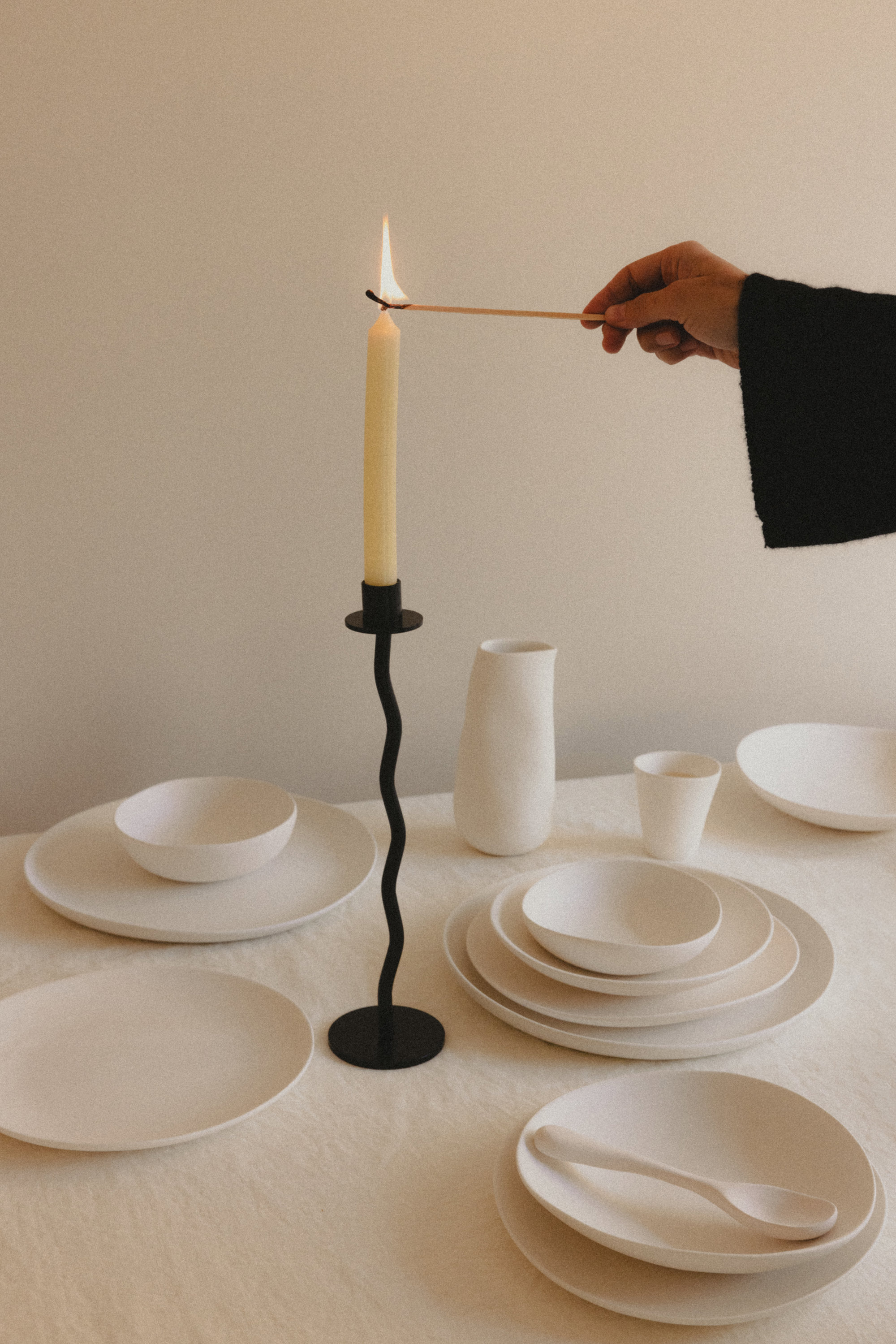 mano encendiendo una vela en una mesa con vajilla blanca