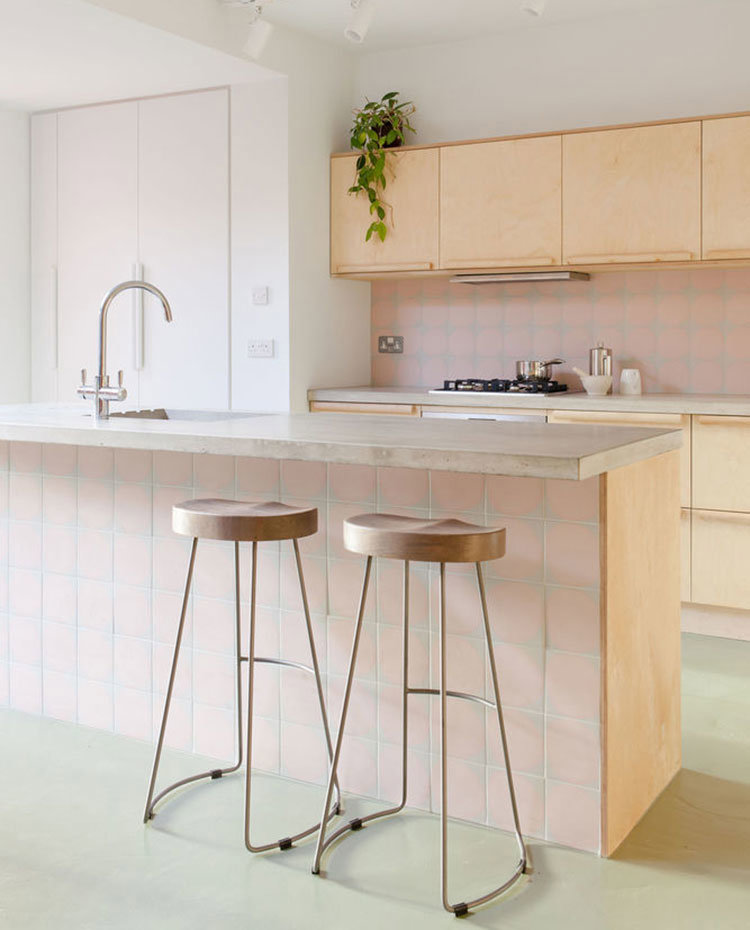 Isla de cocina con voladizo en forma de office, encimera de hormigón, taburetes grises con estructura tubular, planta sobre muebles altos cocina