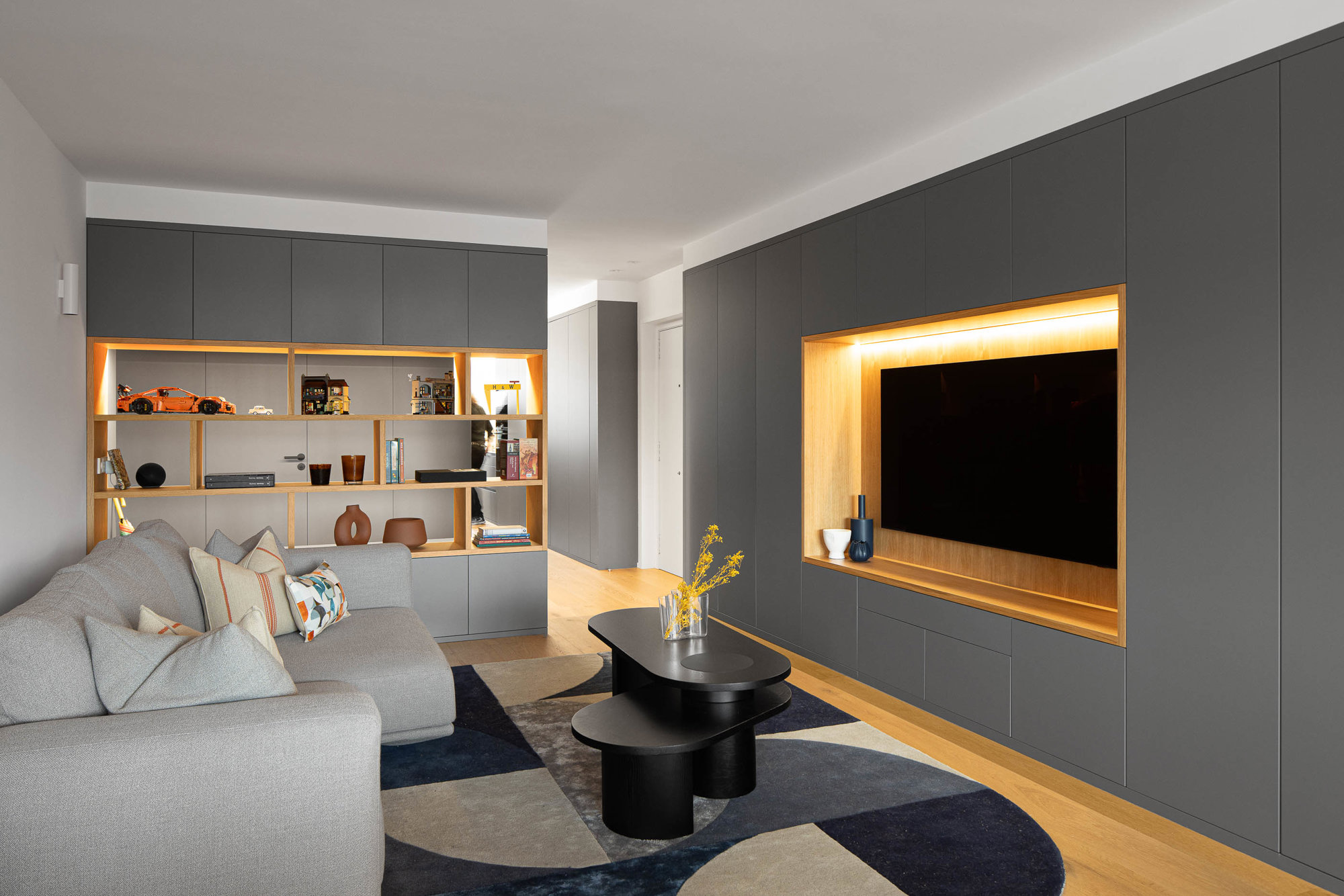 Zona de estar  con sofá gris y pared gris con televisor empotrado