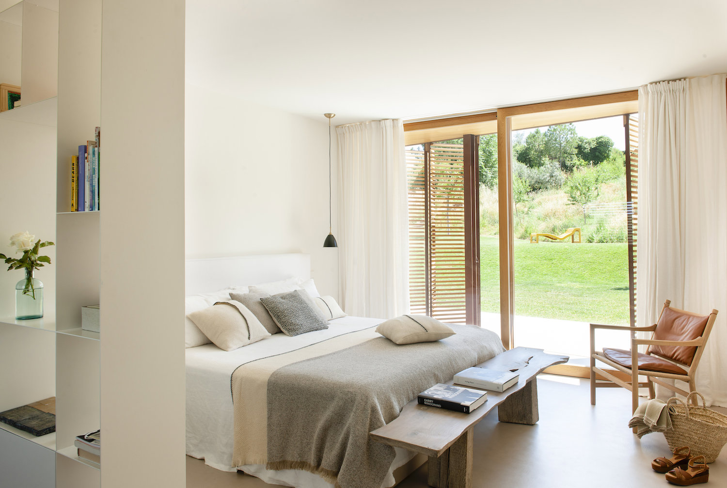 Dormitorio con ropa de cama natural, banco de madera y ventana abierta al jardín