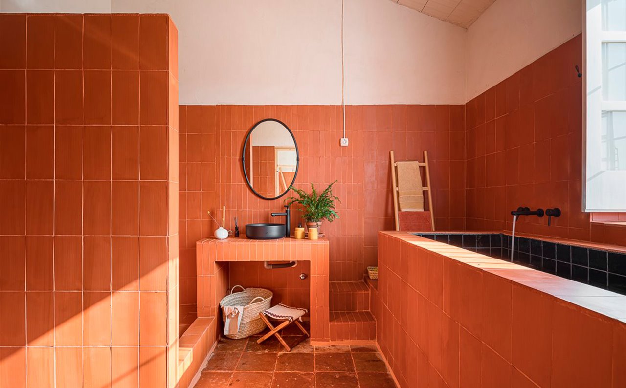 Baño monocromático en color terracota con espejo ovalado y lavabo negro