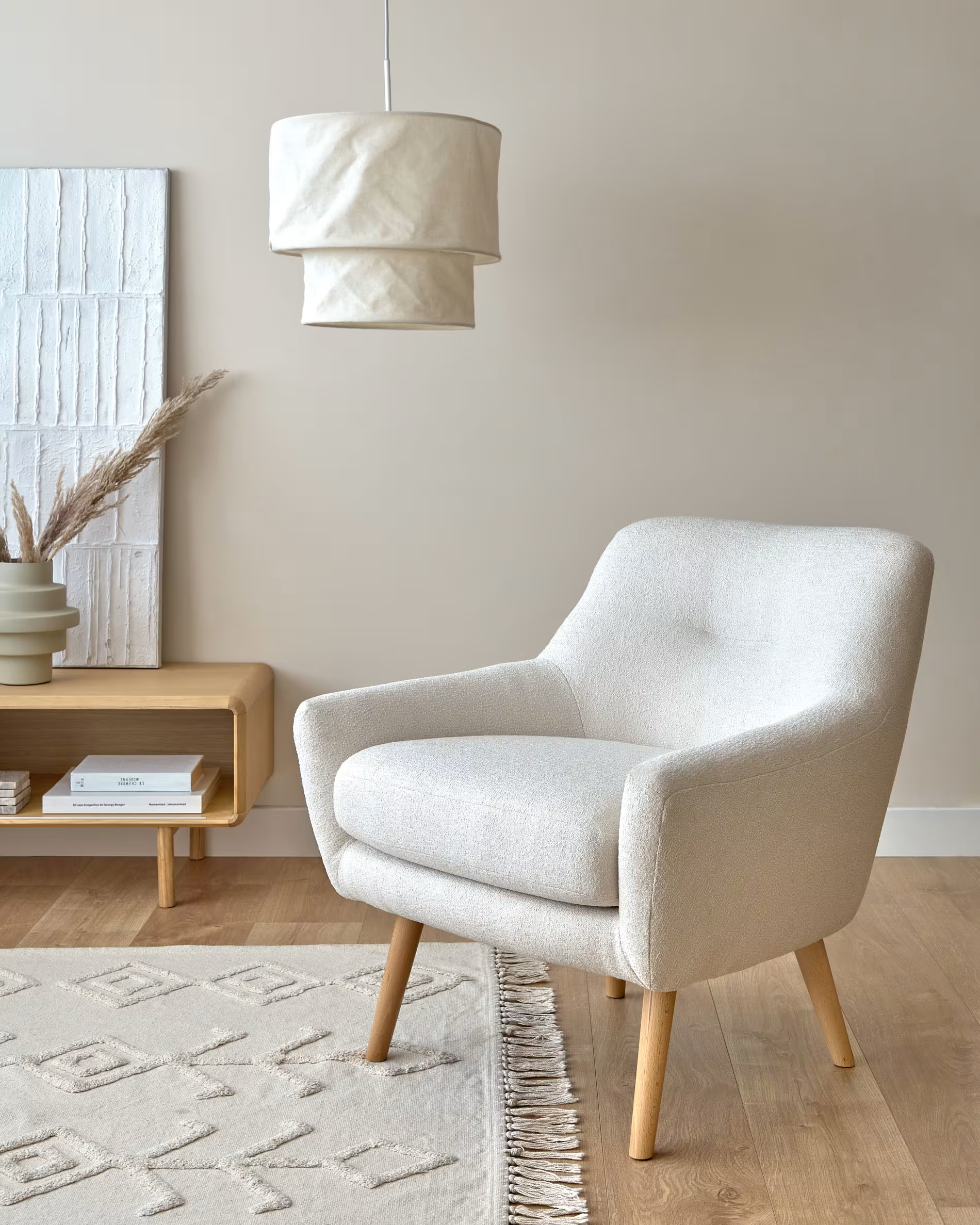 Salón nórdico con lámpara de techo de pantalla de tela blanco crudo sobre sofá individual del mismo color alfombra texturizada en color crema