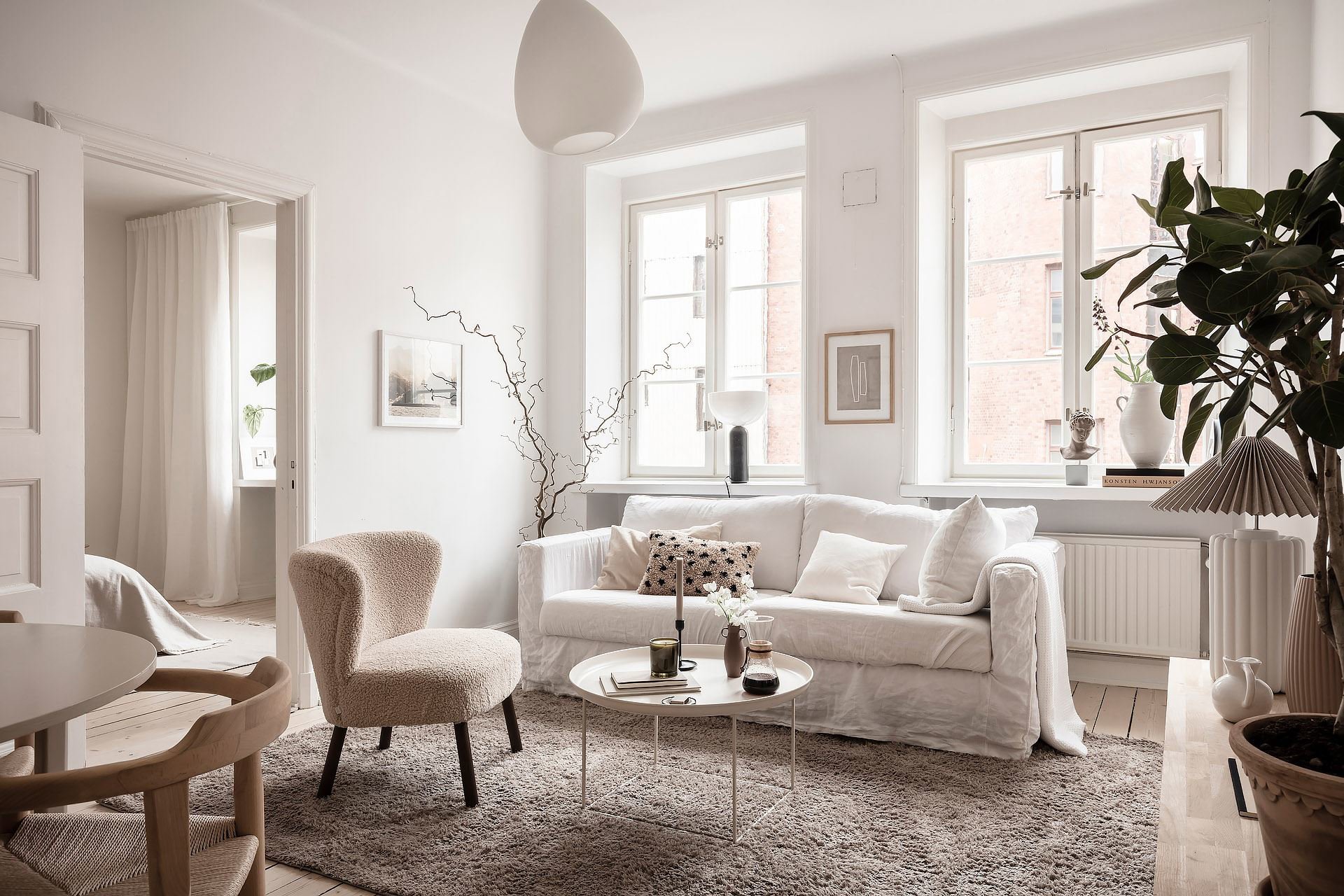 Salón de casa en Suecia con colores blancos, texturas y plantas grandes. Cuenta con buena iluminación, típico de los salones nórdicos. 