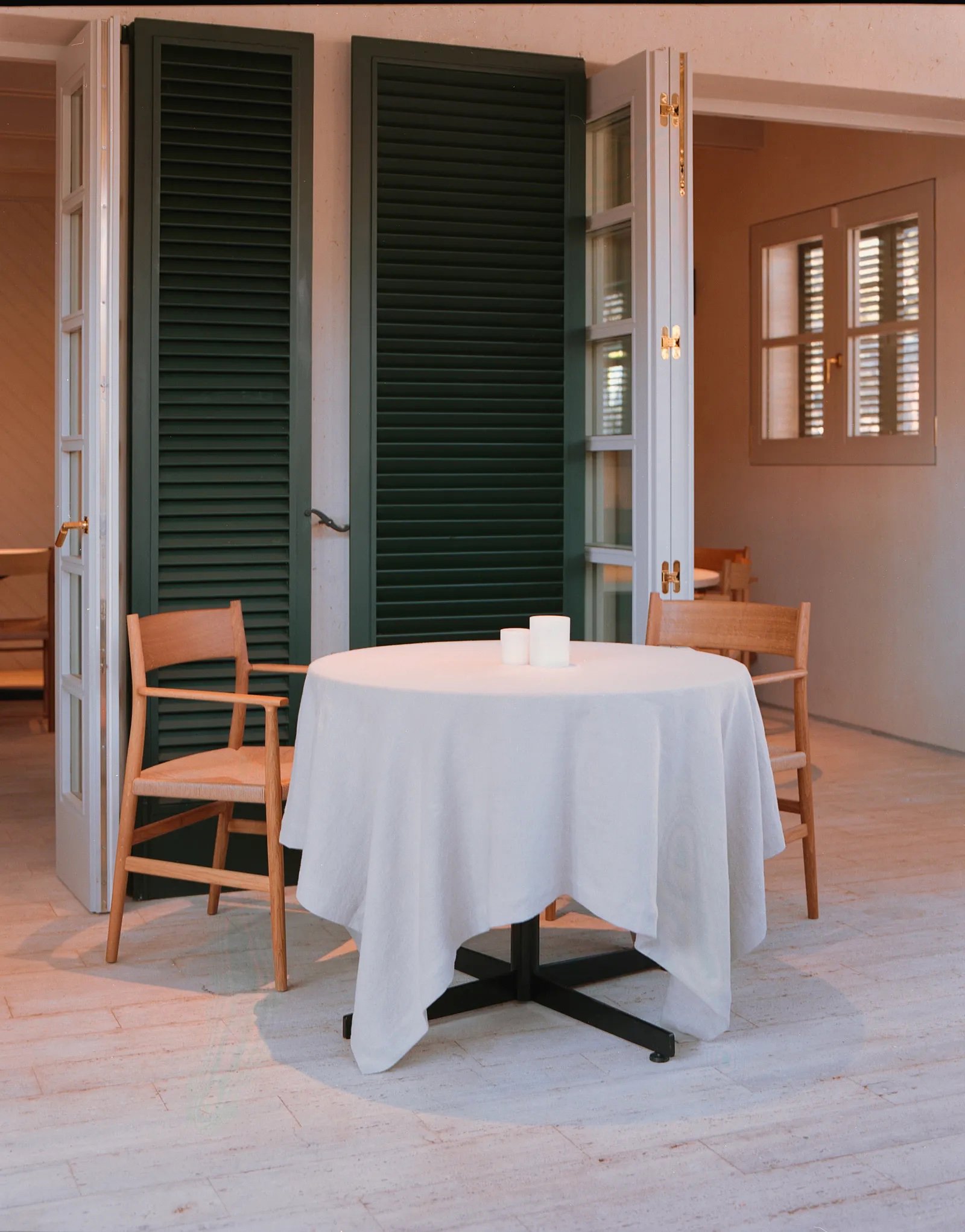 Contraventanas verde, suelo baldosa, mesa con mantel blanco