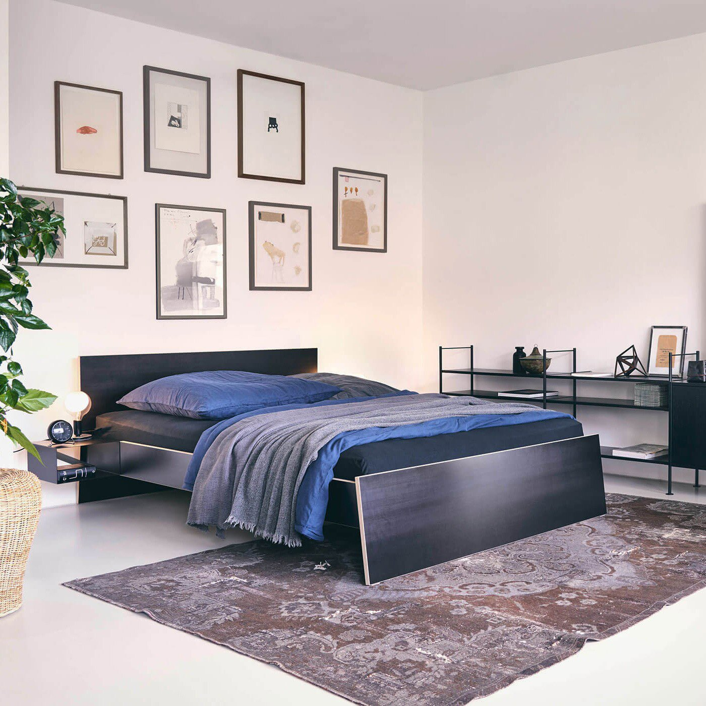 Habitación dormitorio luminosa con alfombra marrón moderna cama en negro y azul y composición de cuadros de diversas medidas en el respaldo