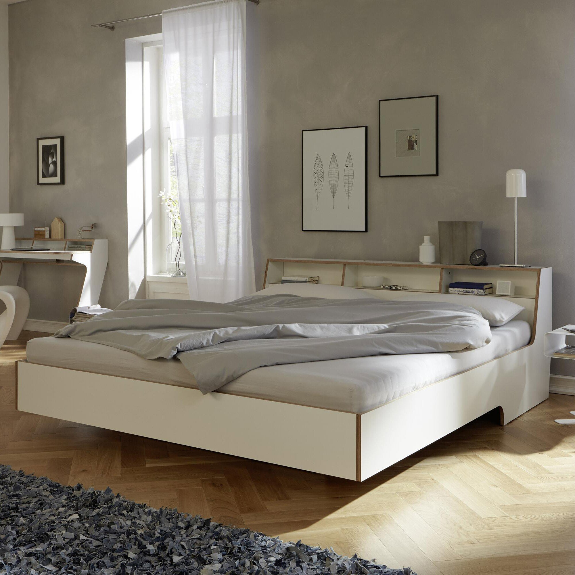 Habitación de dormitorio luminosa con piso de madera cama blanca y dos cuadros colgados sobre el respaldo