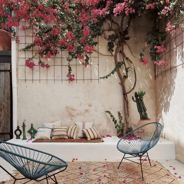 patio mediterráneo con buganvilla, banco de obra blanco, butacas azules, alfombra marroquí