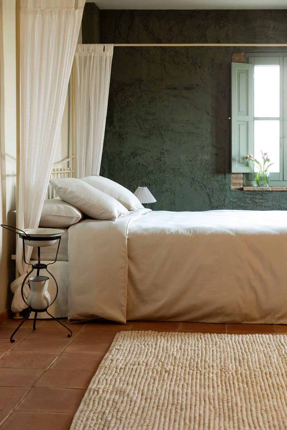 Dormitorio rústico con pared de acento en verde oscuro y cama blanca con alfombra beige y suelo de arcilla