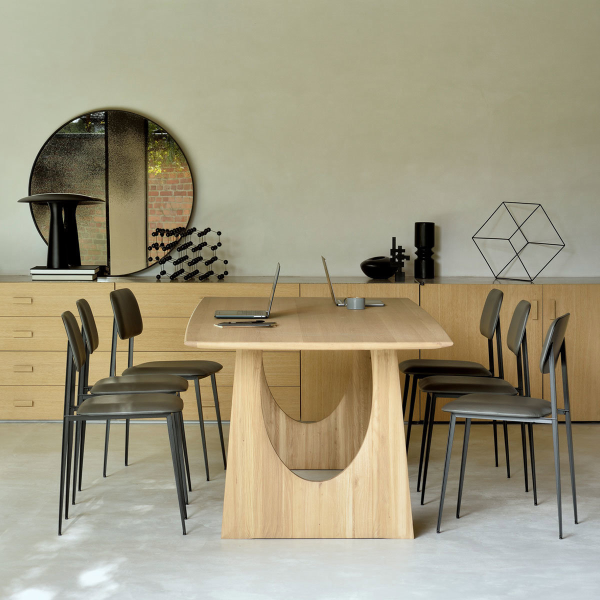 Mesa de comedor rectangular de diseño geométrico. Hecha de madera y rodeada de sillas negras.