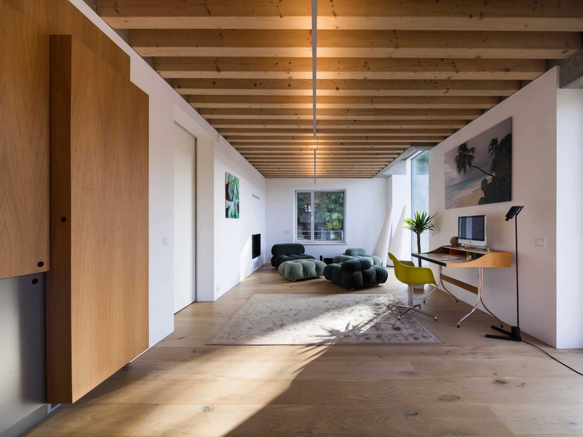 Salón con sofás modulares verde, alfombra en el centro y escritorio de madera