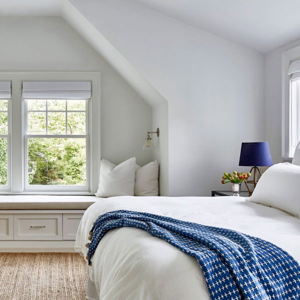 Dormitorio blanco con silla de mimbre y ropa de cama azul y blanca