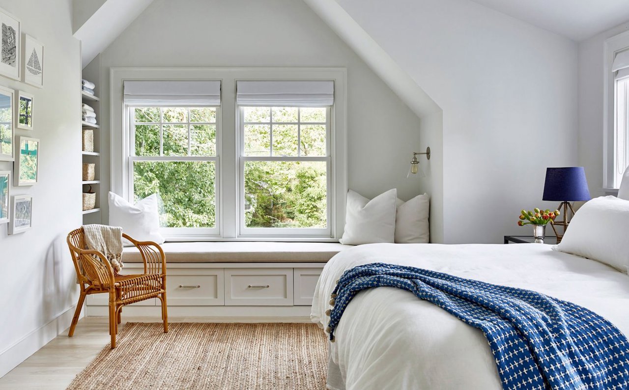 Dormitorio blanco con silla de mimbre y ropa de cama azul y blanca