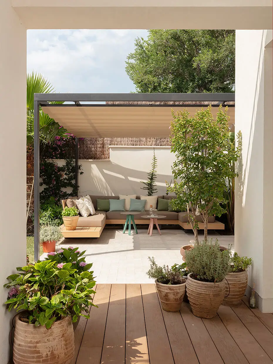 Terraza con alfombra blanca y macetas llenas de plantas. Sofá sobre madera en color gris.