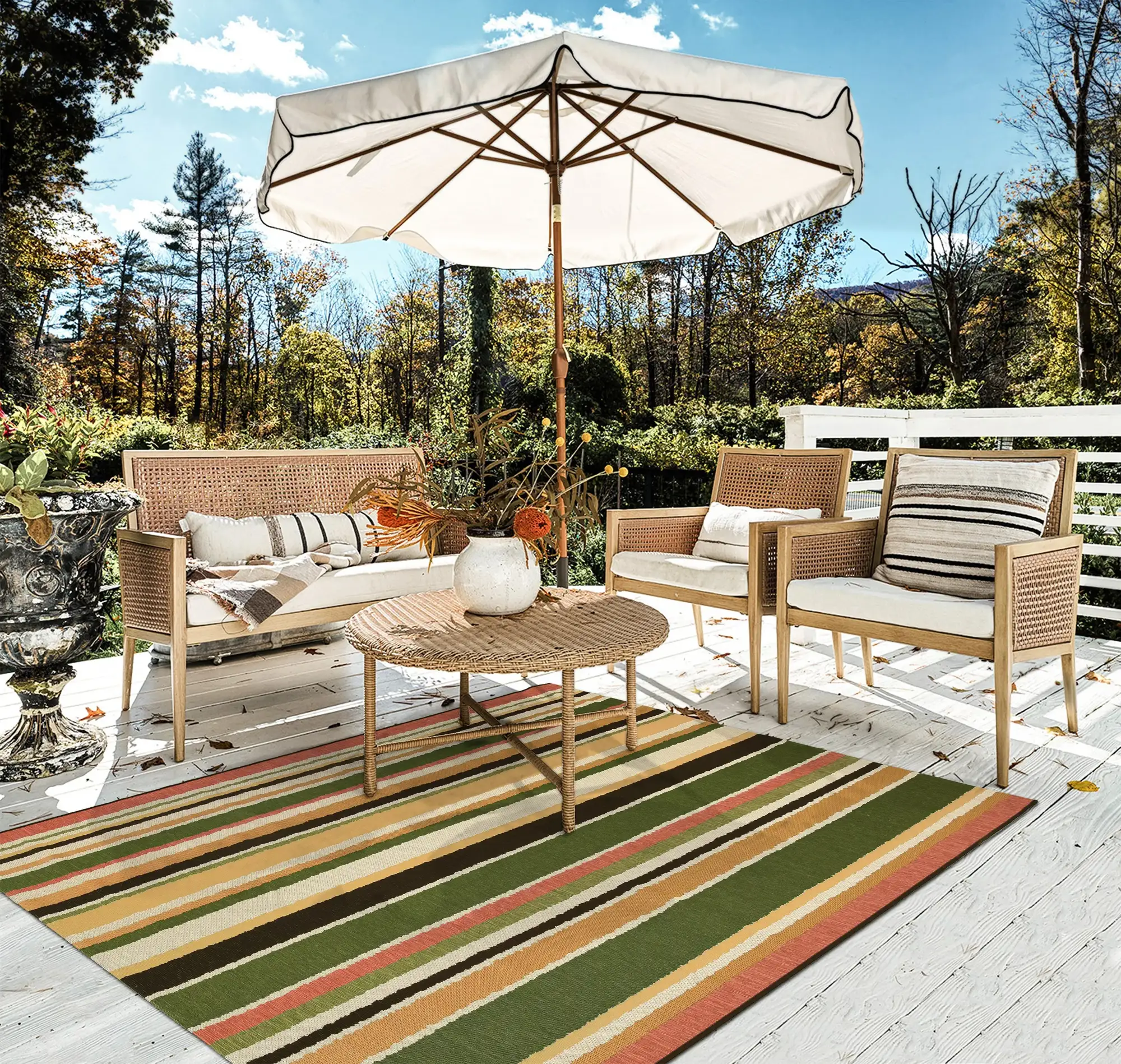 Alfombra de rayas en colores vivos verde, amarillo, coral y crema. La terraza está compuesta por dos sillas y un sillón de fibras naturales y una mesa de centro redonda. 