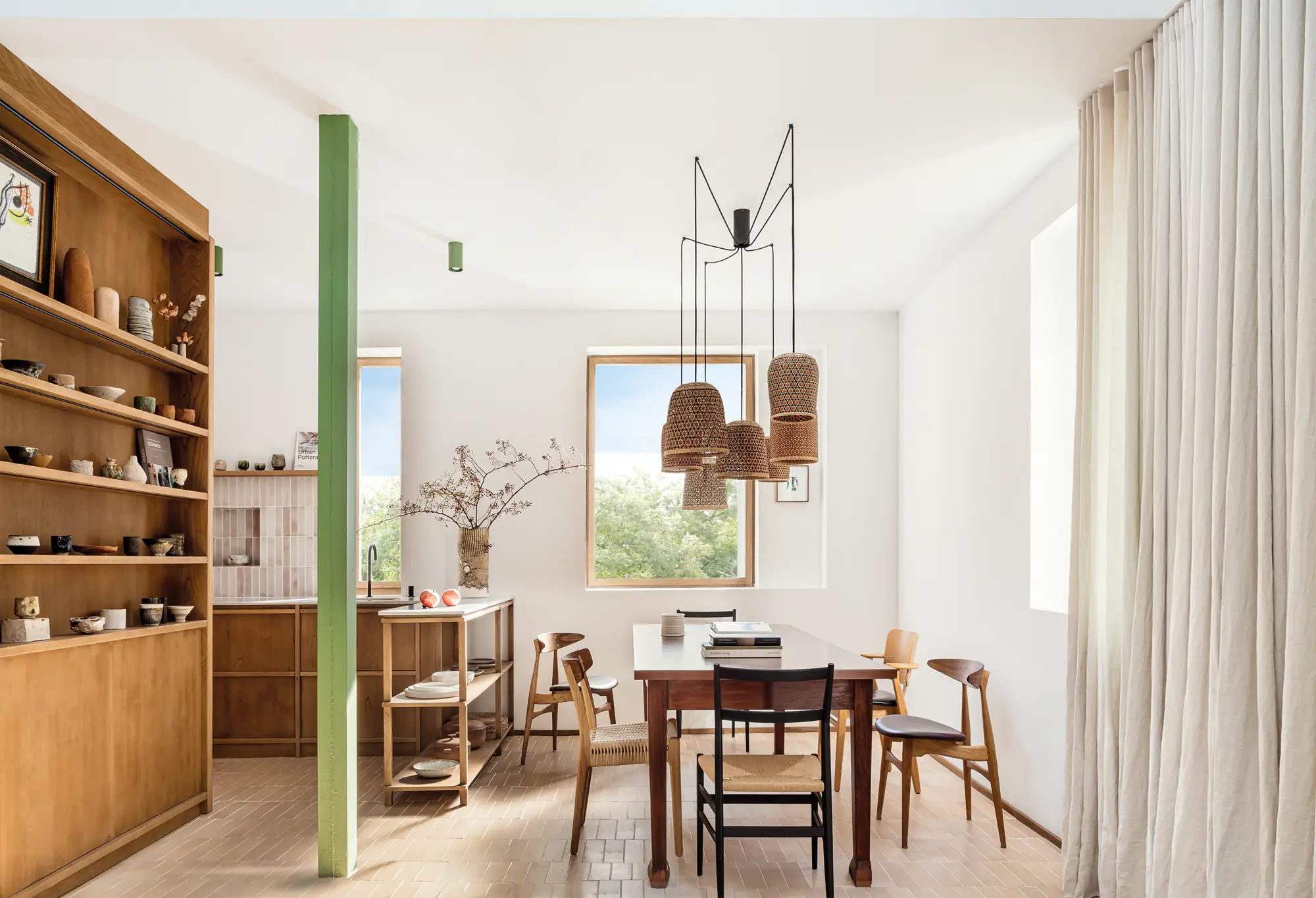 Comedor luminoso con pilar de color verde que separa la cocina y la mesa de comedor. Muebles de madera. 