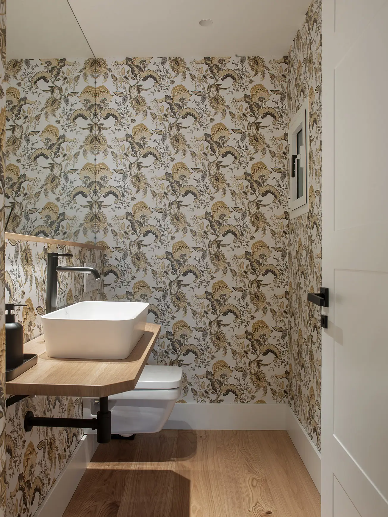 Baño de casa de Arquitectura y Diseño con papel pintado con motivos botánicos, encimera de madera, lavabo blanco cuadrado, grifo alto e inodoro.