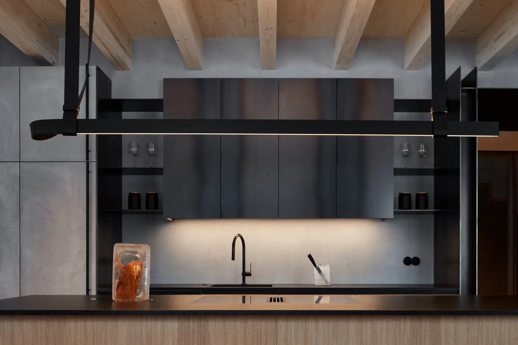 Cocina con luces negras, mueble de acero y encimera de mármol negro. Base de madera y techo de madera con vigas expuestas. 