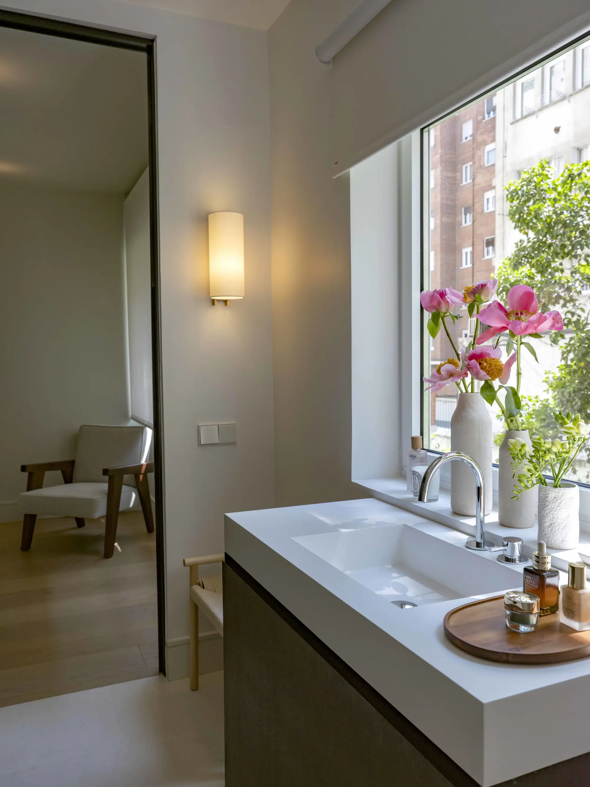 Baño con vistas, mueble de madera, encimera blanca, decoración con flores y plantas. 