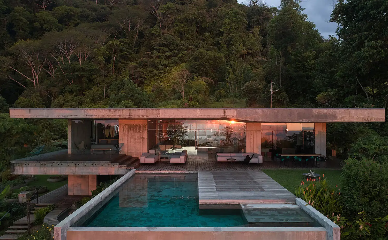 Vista exterior al atardecer desde la piscina con estructura de hormigón y cerramientos de cristal