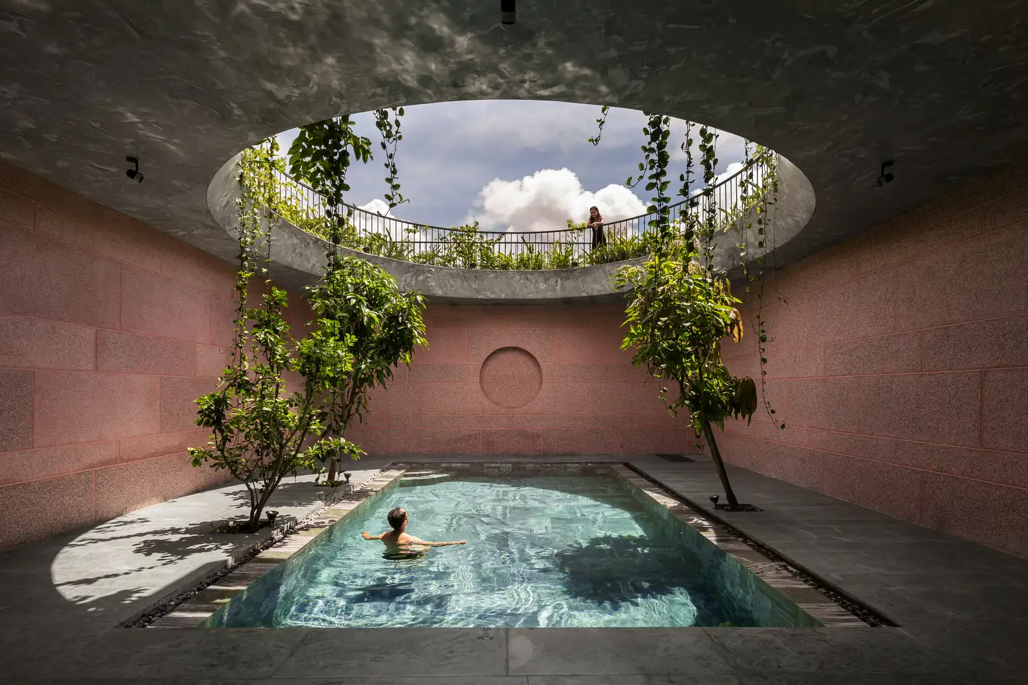 Piscina de casa rosa en Vietnam rodeada de árboles y bajo un círculo abierto al cielo.