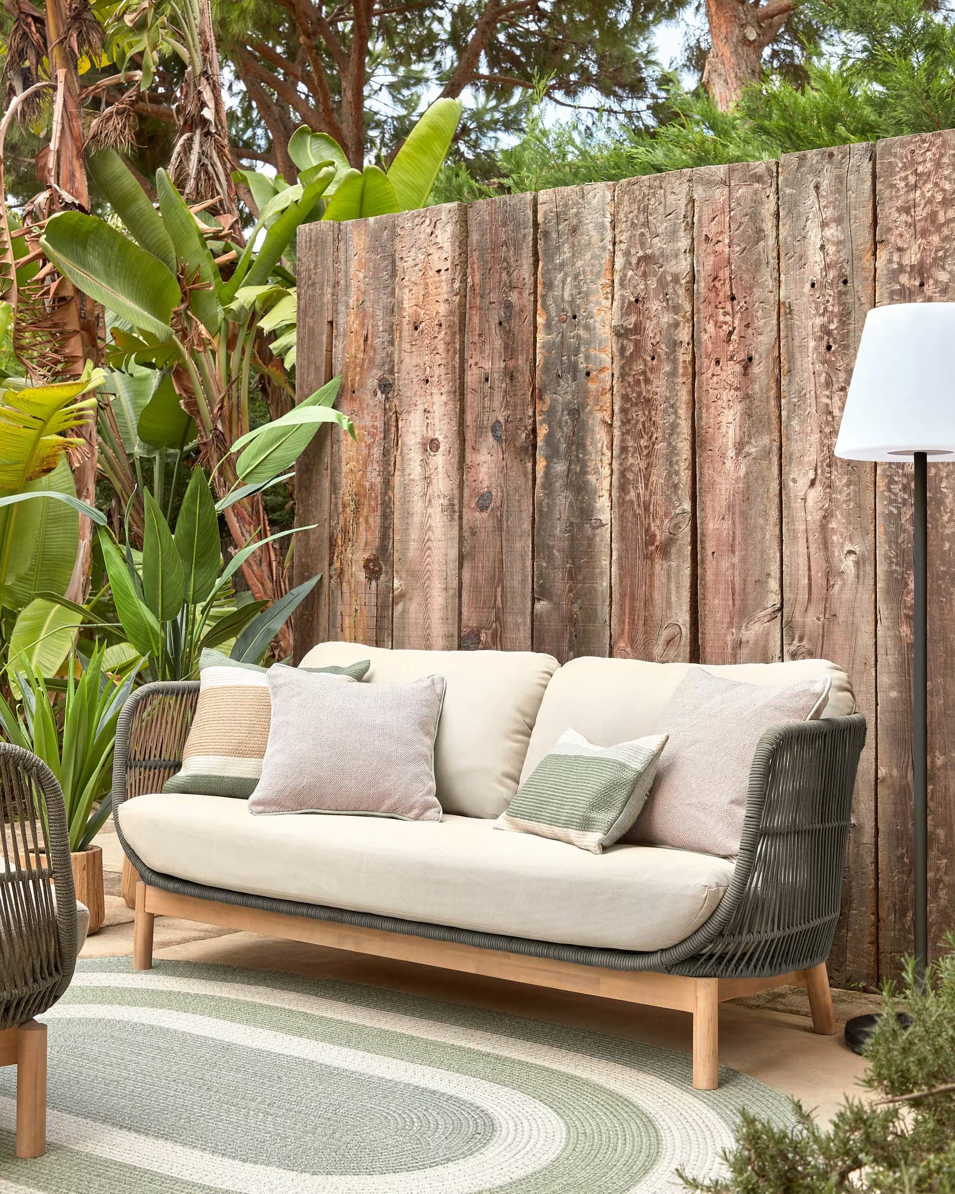 Terraza descubierta con sofá beige, lámpara de pie con pantalla blanca y alfombra verde con blanco. 