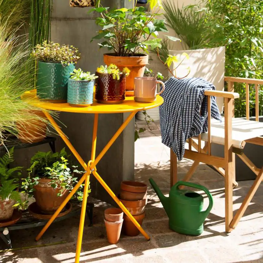 Mesa amarilla plegable con plantas en su superficie en jardín luminoso. 