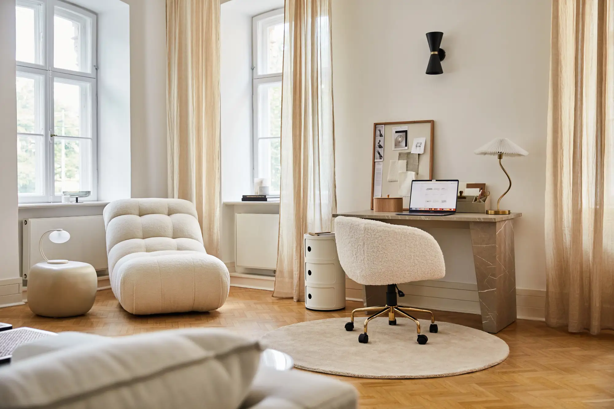 Salón luminoso con suelo de madera, alfombra redonda blanca, espacio de trabajo con silla giratoria y escritorio de mármol gris. 