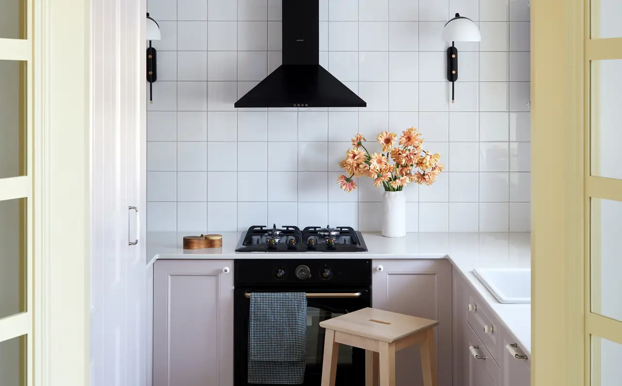 Esta cocina pequeña está llena de detalles, como los apliques, los armarios bajos en tono rosa y los tiradores de aire 'vintage'.