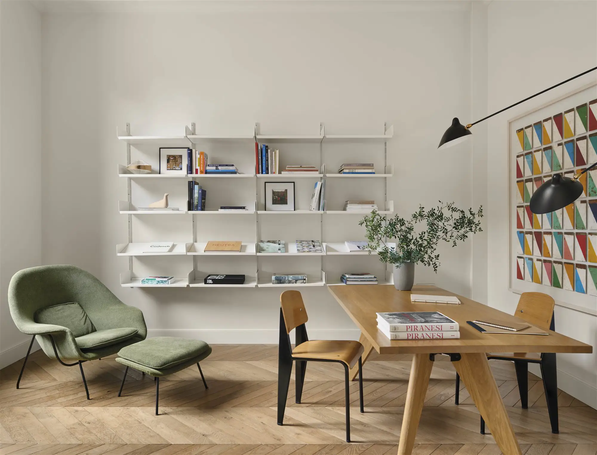 Salón blanco contemporáneo con toques de color y estantería flotante. Mesa de comedor de madera robusta y butaca con otomana.