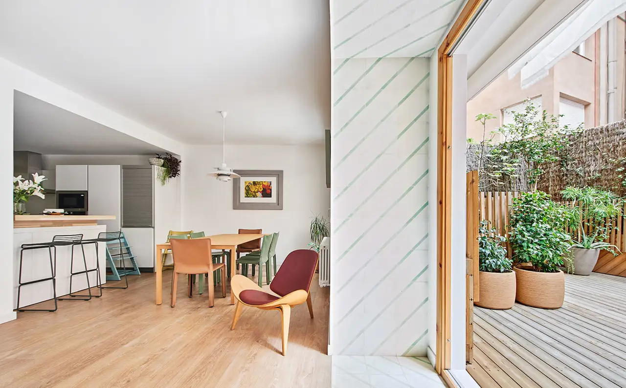 Comedor y zona de office de cocina junto a butaca da madera con piel granate y apertura hacia exterior revestida de cerámica.