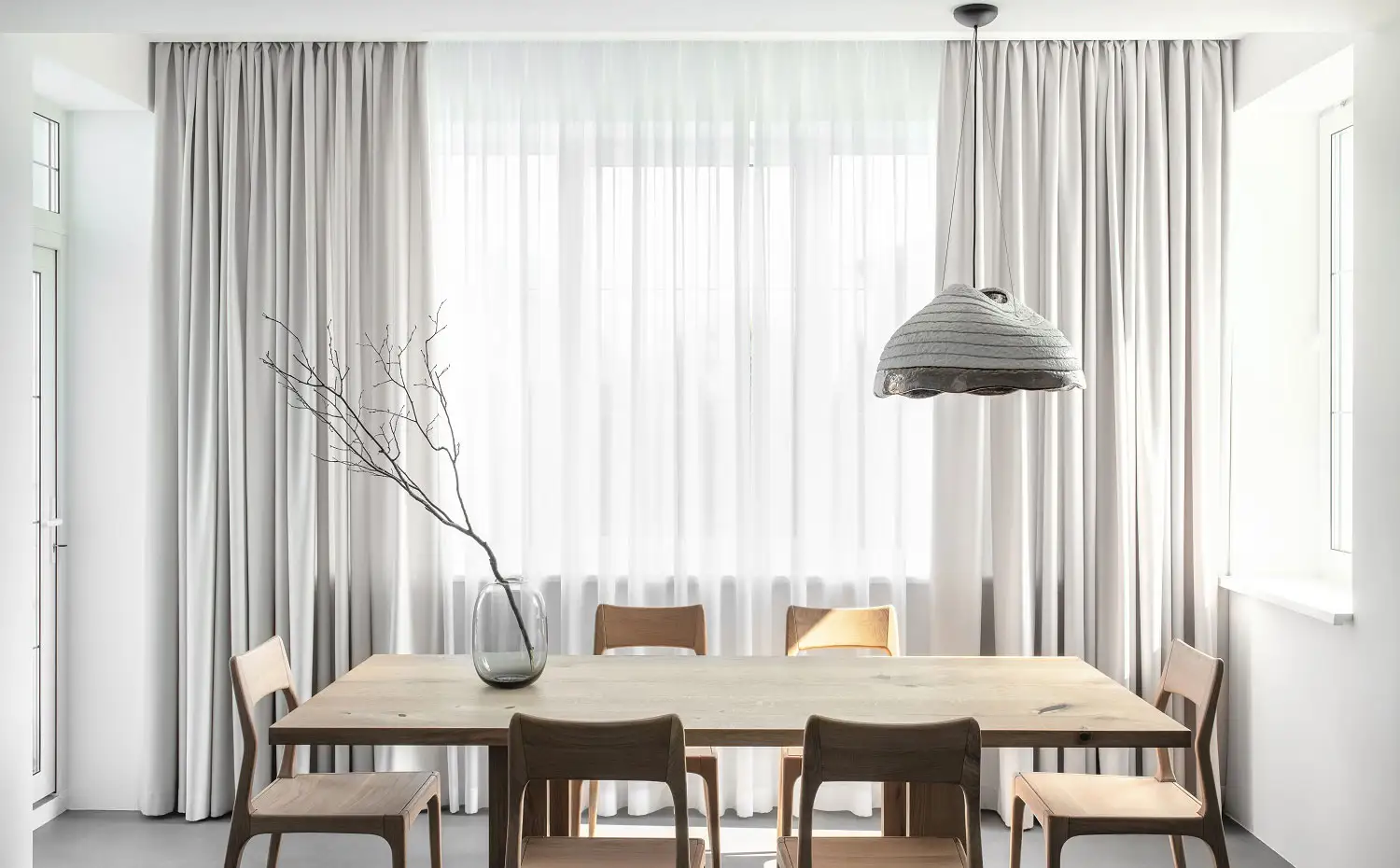 Mesa de comedor con sillas a juego, jarrón de cristal, cortinas en gris claro