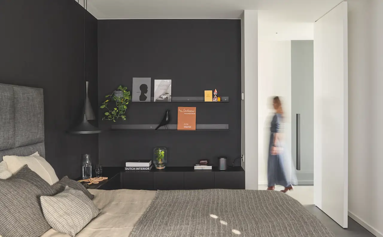 Dormitorio con cabecero de tela de colro gris y paredes pintadas de color negro