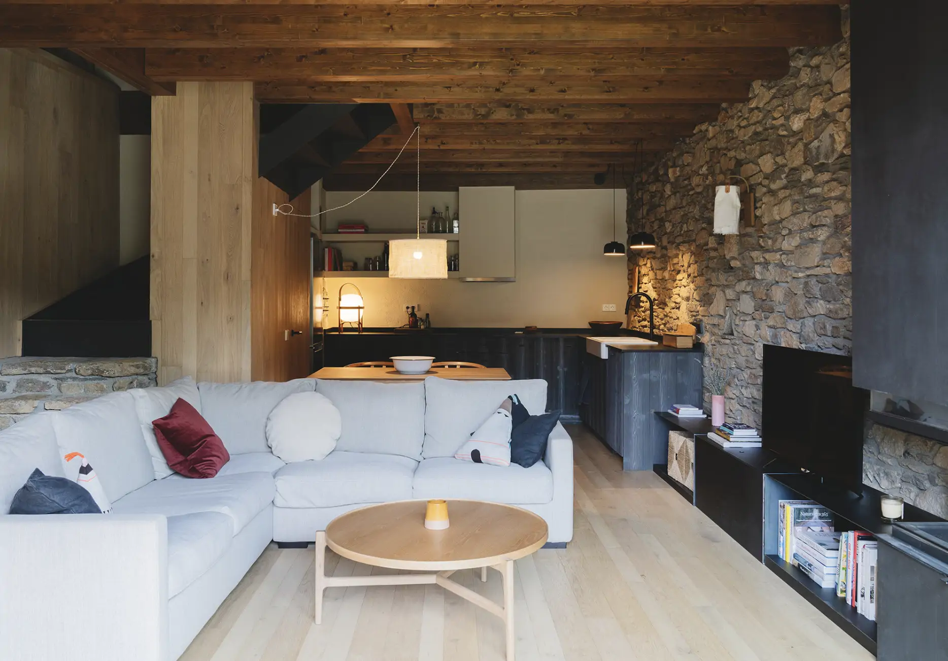 sofa blanco con cocina al fondo y pared de piedra